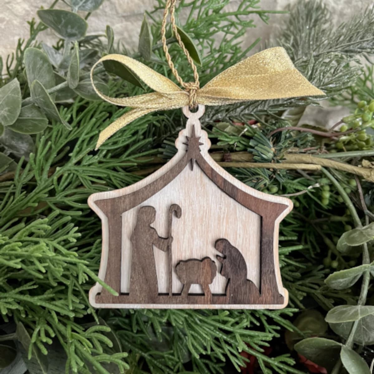 Wooden Christmas ornament depicting Mary, Joseph, and Baby Jesus lying in a manger.